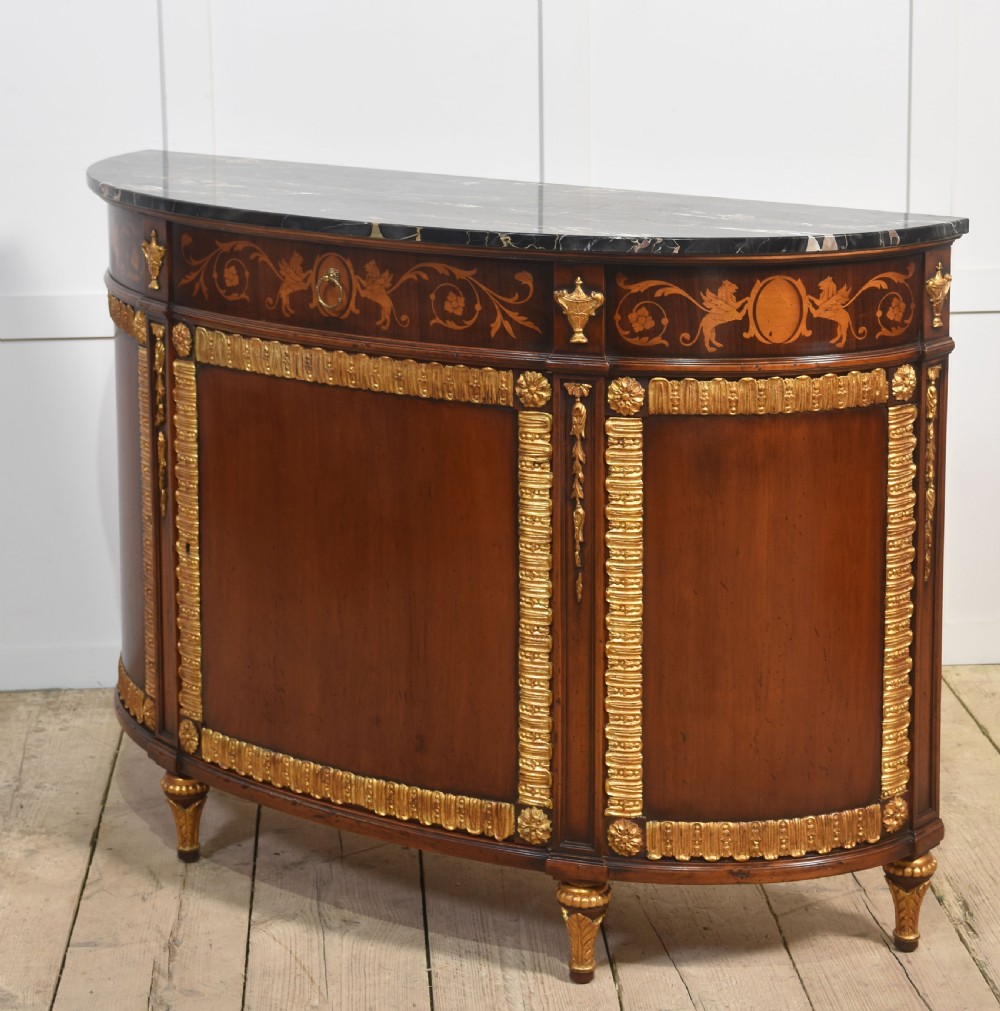 An Italian Neoclassical mahogany bowfront cabinet featuring a black marble top, marquetry frieze with foliate motifs, and carved parcel gilt trims. View XI