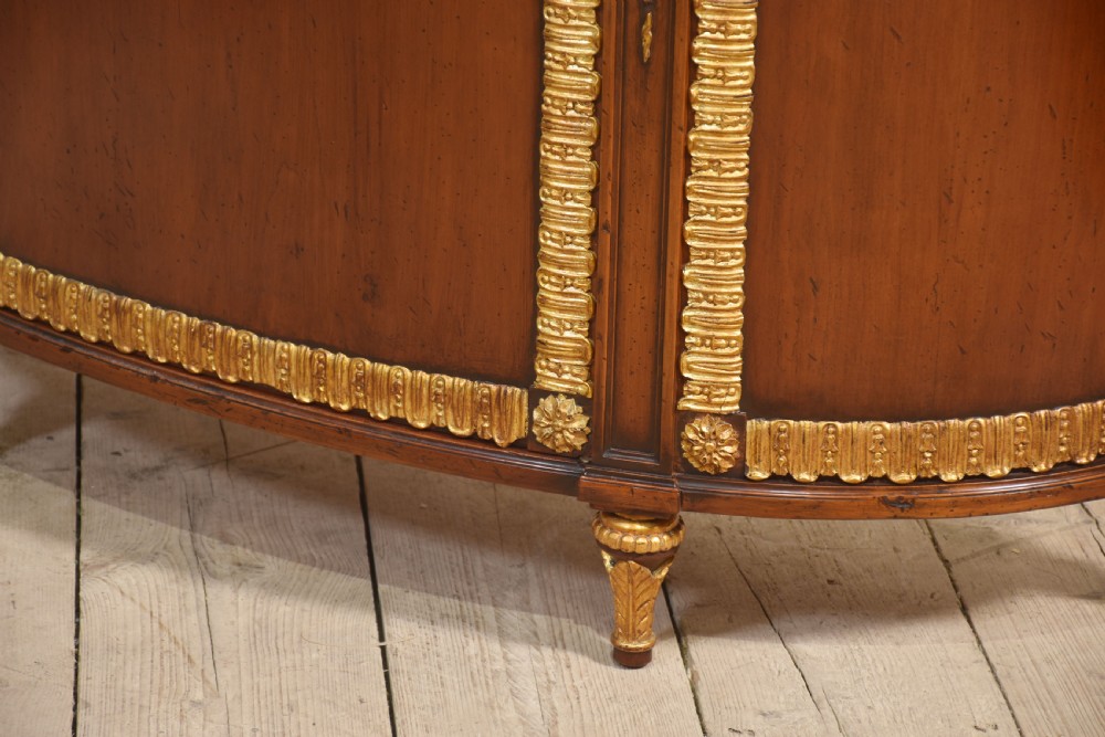 An Italian Neoclassical mahogany bowfront cabinet featuring a black marble top, marquetry frieze with foliate motifs, and carved parcel gilt trims. View XII
