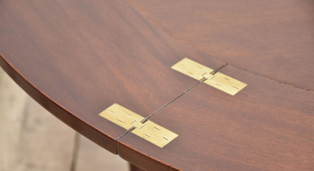 A dark mahogany circular dining table featuring outer leaf extension segments connected with brass hinges and supported by four fluted legs. View VIII