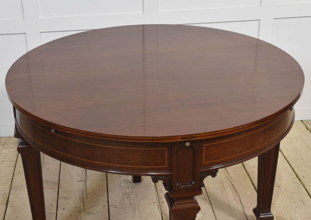 A dark mahogany circular dining table featuring outer leaf extension segments connected with brass hinges and supported by four fluted legs. View XIV