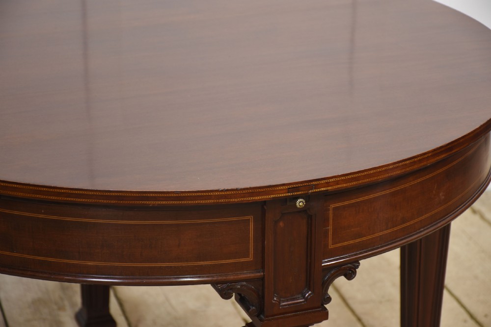 A dark mahogany circular dining table featuring outer leaf extension segments connected with brass hinges and supported by four fluted legs. View XVI