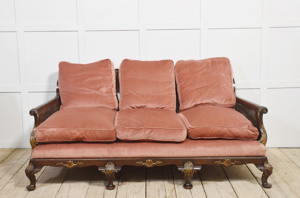 A three-seater carved walnut sofa featuring caned panels, parcel-gilt shell carved details, cabriole legs, and three rose-pink velvet seat cushions. View II