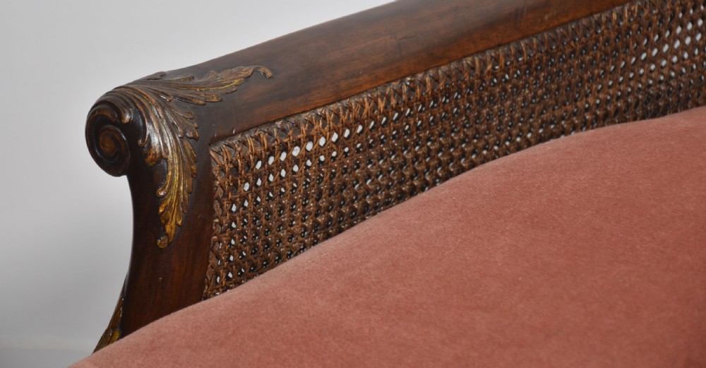 A three-seater carved walnut sofa featuring caned panels, parcel-gilt shell carved details, cabriole legs, and three rose-pink velvet seat cushions. View V