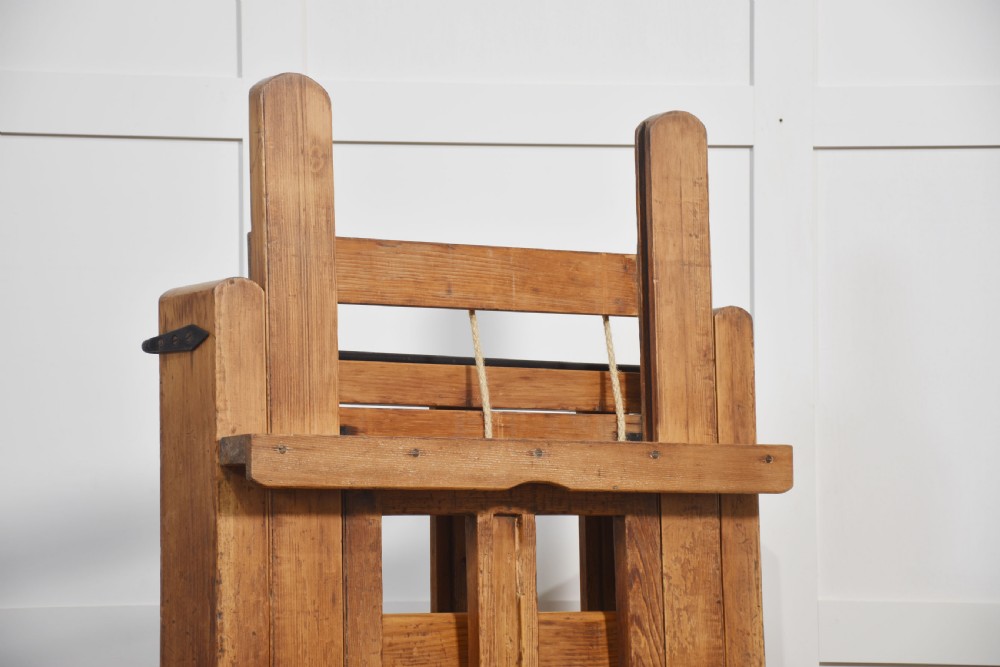 A large antique wooden artist studio easel with a crank handle mechanism standing on a pale wooden floor. View VII