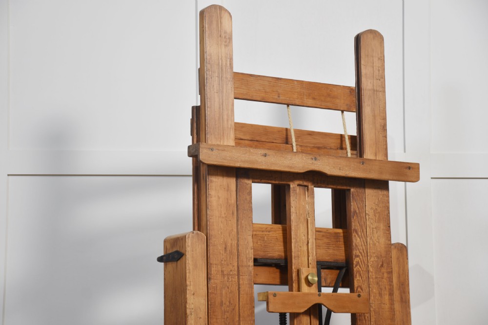 A large antique wooden artist studio easel with a crank handle mechanism standing on a pale wooden floor. View IX