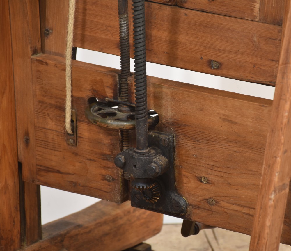 A large antique wooden artist studio easel with a crank handle mechanism standing on a pale wooden floor. View XX