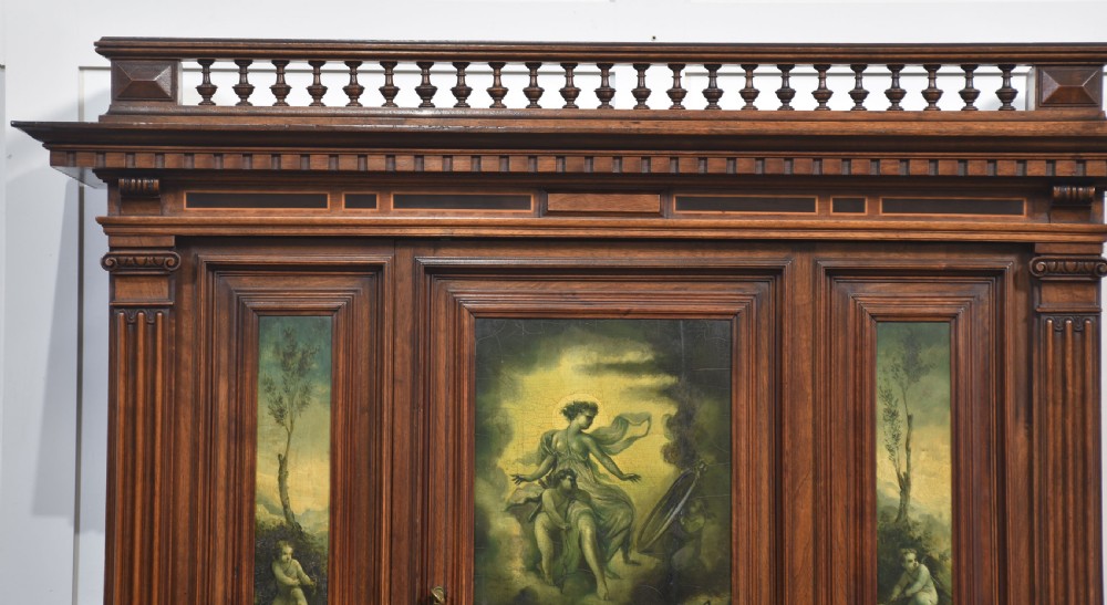 A two-tier dark walnut cabinet on stand featuring classical relief carvings, painted figural panels, fluted columns, and a top balustrade gallery. View III