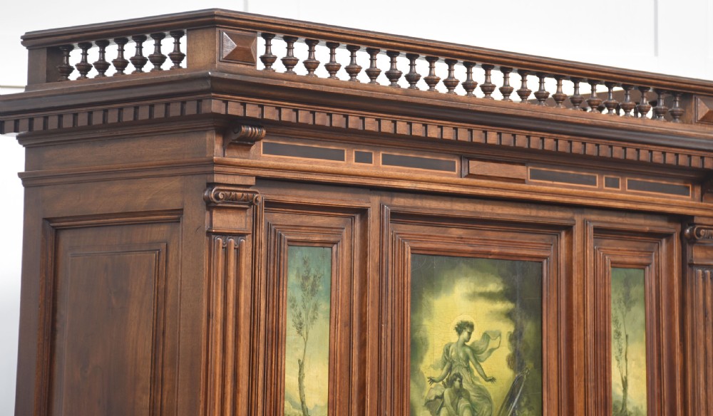 A two-tier dark walnut cabinet on stand featuring classical relief carvings, painted figural panels, fluted columns, and a top balustrade gallery. View X