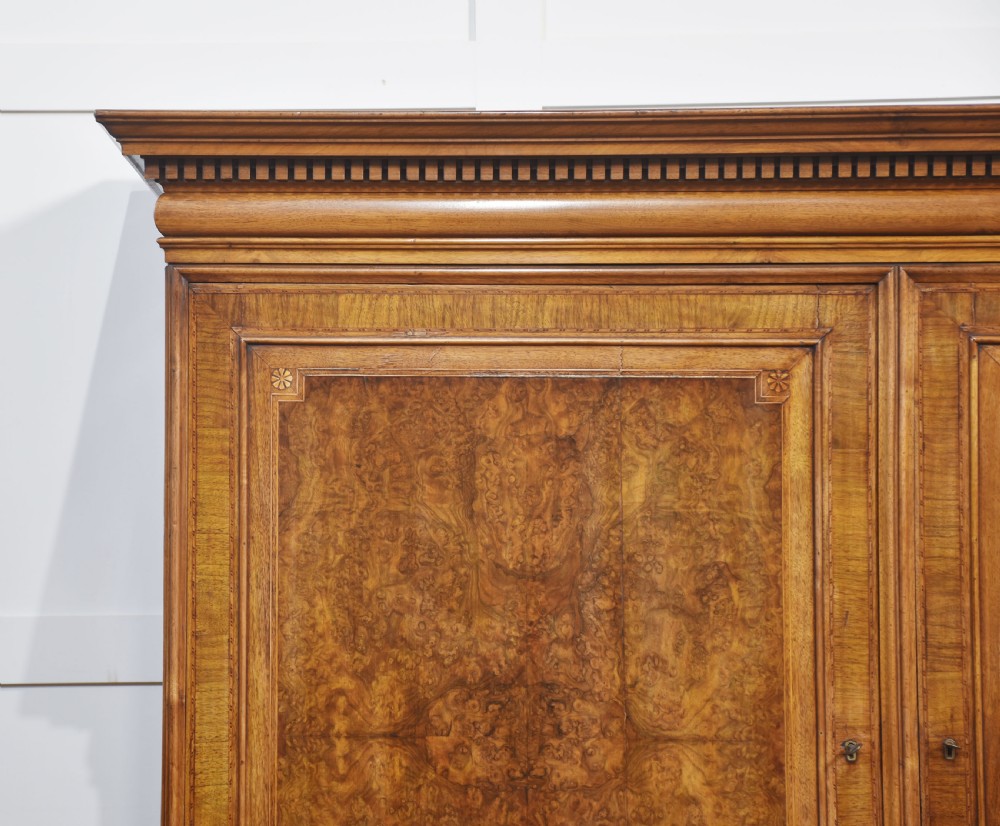 A two-section figured walnut press cupboard featuring twin panelled doors with crossbanded borders and bracket feet with a central star inlay. View II