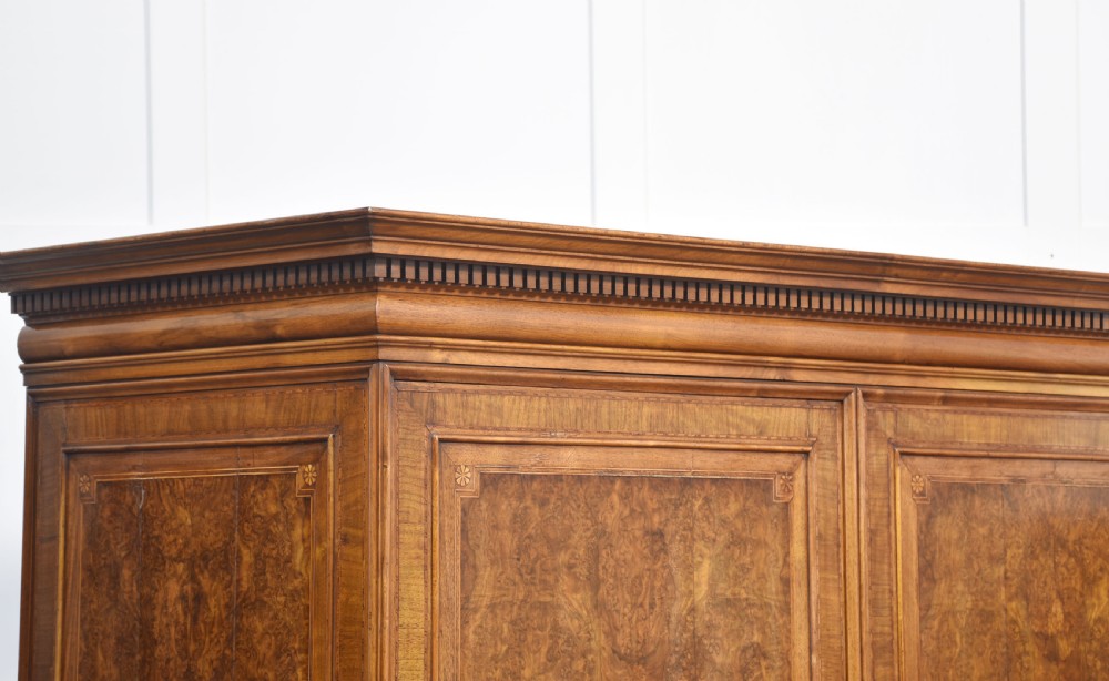 A two-section figured walnut press cupboard featuring twin panelled doors with crossbanded borders and bracket feet with a central star inlay. View VIII