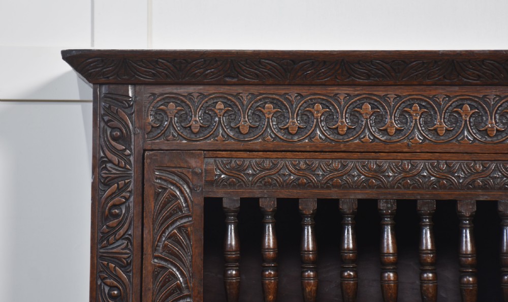 A wall-mounted 17th-century dark oak mural livery cupboard featuring hand-carved borders, turned wooden spindles, and brass hardware. View III