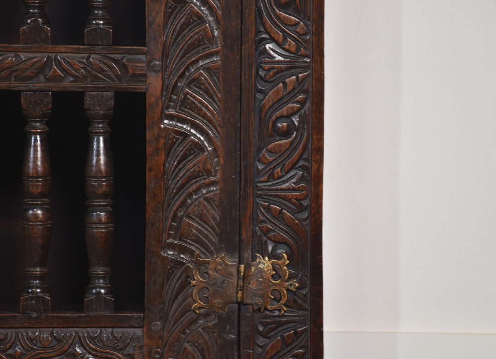 A wall-mounted 17th-century dark oak mural livery cupboard featuring hand-carved borders, turned wooden spindles, and brass hardware. View VII