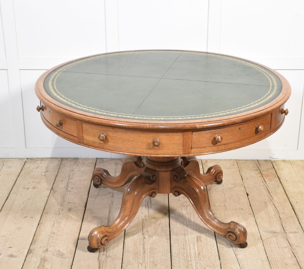 A 19th-century circular oak drum table featuring a green leather inset top with gilt tooling, multiple frieze drawers, and a turned pedestal on scroll legs with brass castors. View II