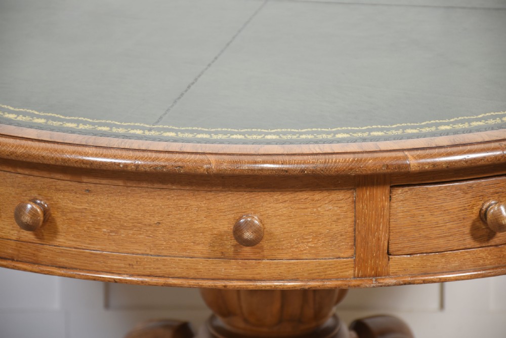 A 19th-century circular oak drum table featuring a green leather inset top with gilt tooling, multiple frieze drawers, and a turned pedestal on scroll legs with brass castors. View III