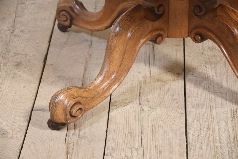 A 19th-century circular oak drum table featuring a green leather inset top with gilt tooling, multiple frieze drawers, and a turned pedestal on scroll legs with brass castors. View VI