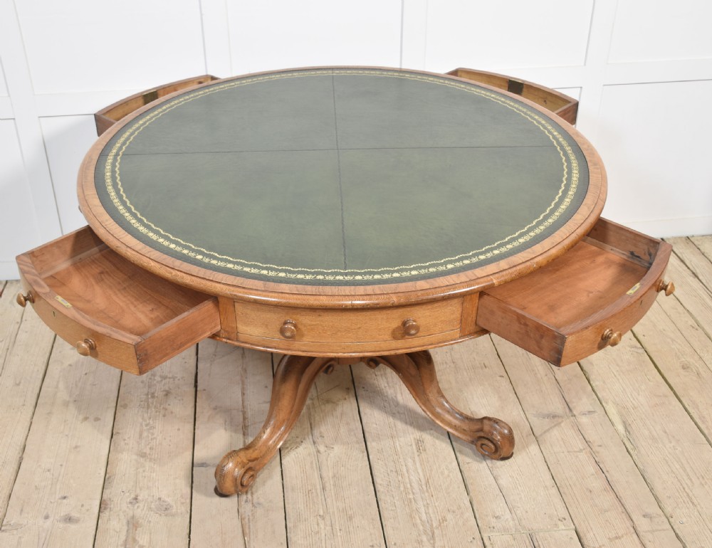 A 19th-century circular oak drum table featuring a green leather inset top with gilt tooling, multiple frieze drawers, and a turned pedestal on scroll legs with brass castors. View VII