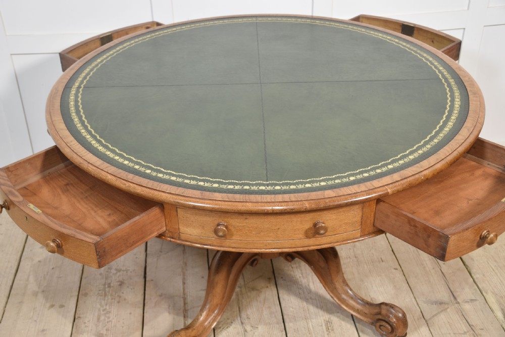 A 19th-century circular oak drum table featuring a green leather inset top with gilt tooling, multiple frieze drawers, and a turned pedestal on scroll legs with brass castors. View IX