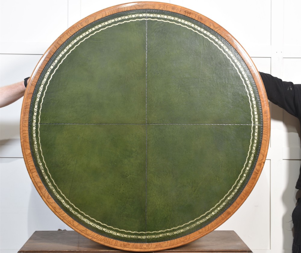 A 19th-century circular oak drum table featuring a green leather inset top with gilt tooling, multiple frieze drawers, and a turned pedestal on scroll legs with brass castors. View XII