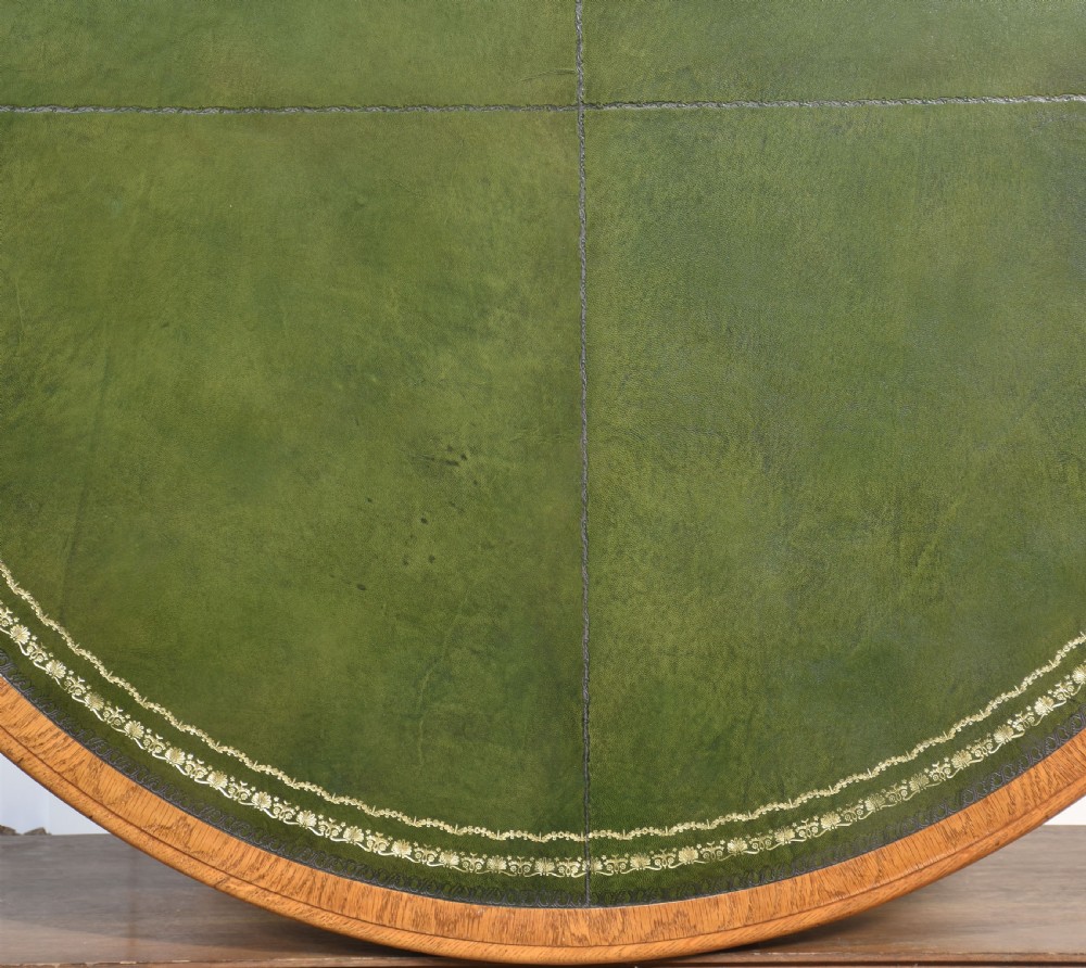 A 19th-century circular oak drum table featuring a green leather inset top with gilt tooling, multiple frieze drawers, and a turned pedestal on scroll legs with brass castors. View XIII