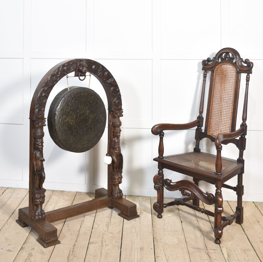 A dark carved oak arched frame featuring a central lion head mask housing a hammered circular brass gong and suspended striking mallet. View III