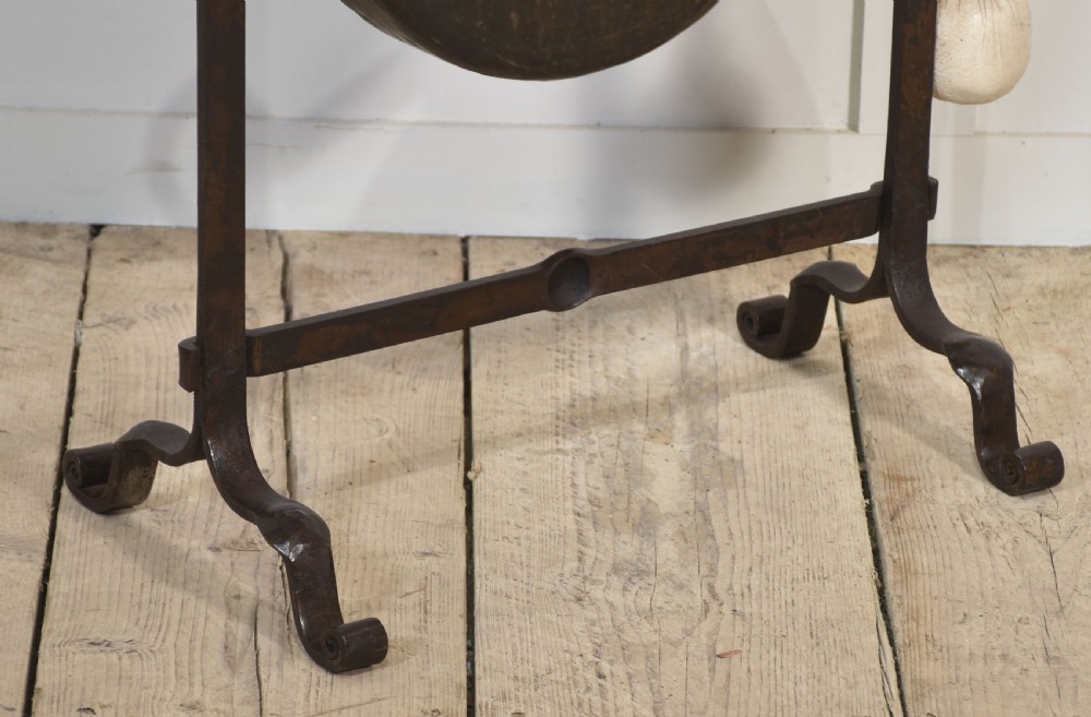 An antique wrought iron standing frame featuring scrolled corners, holding a central hammered metal circular gong suspended by rope with an attached padded striker. View III