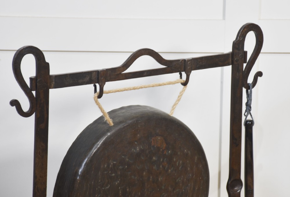 An antique wrought iron standing frame featuring scrolled corners, holding a central hammered metal circular gong suspended by rope with an attached padded striker. View V