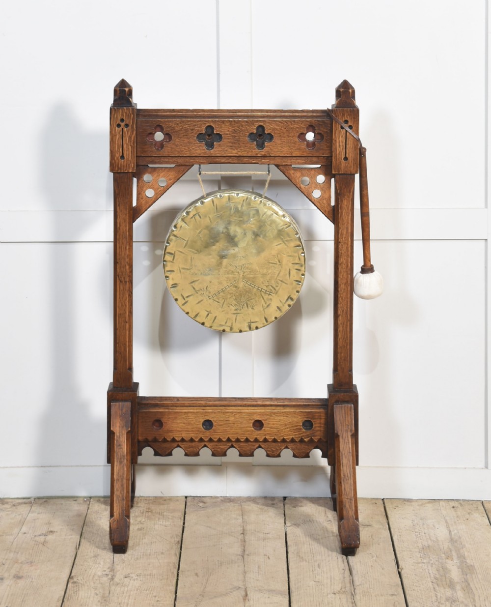 A carved oak freestanding frame in Gothic Revival style housing a central suspended circular brass gong with an attached wooden striker.