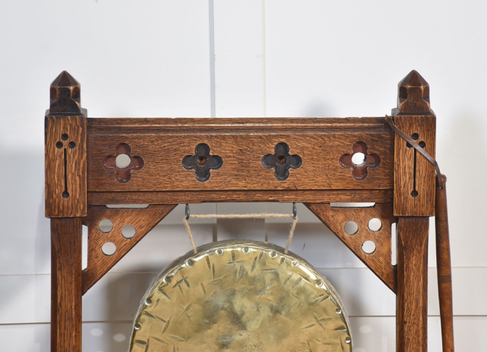 A carved oak freestanding frame in Gothic Revival style housing a central suspended circular brass gong with an attached wooden striker. View III