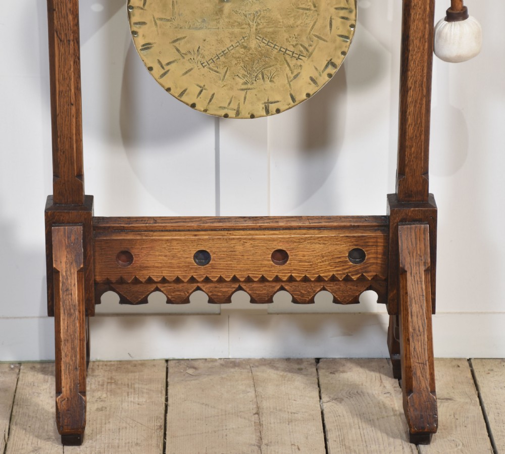 A carved oak freestanding frame in Gothic Revival style housing a central suspended circular brass gong with an attached wooden striker. View VII