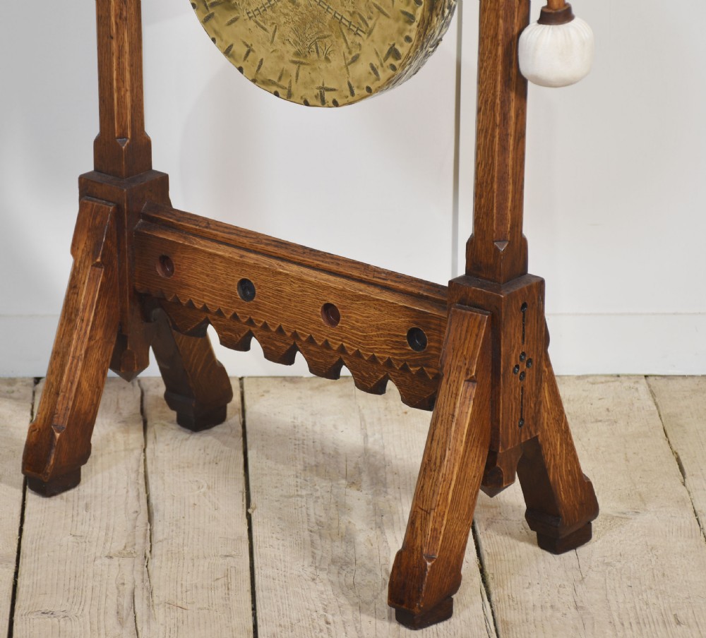 A carved oak freestanding frame in Gothic Revival style housing a central suspended circular brass gong with an attached wooden striker. View XI