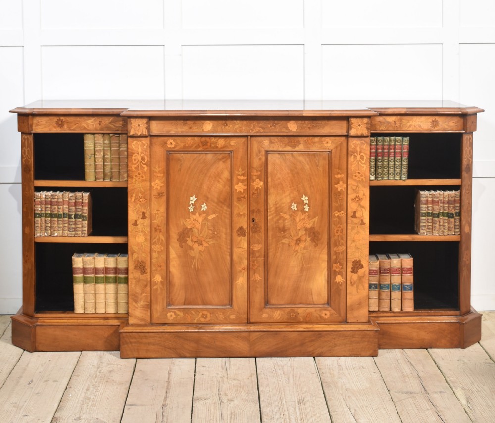 A low antique walnut breakfront bookcase featuring floral marquetry inlay across the central cupboard doors and top frieze, flanked by open adjustable shelves.