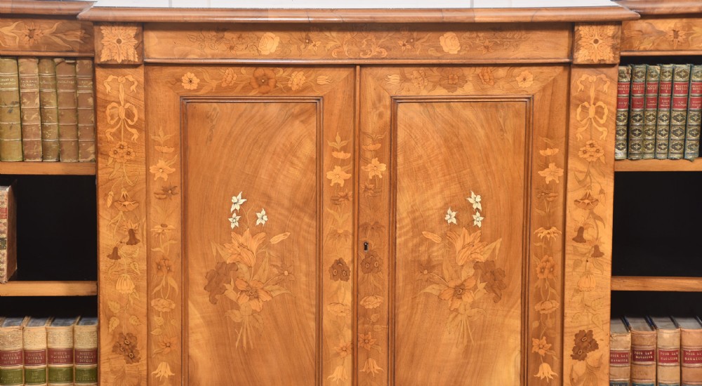 A low antique walnut breakfront bookcase featuring floral marquetry inlay across the central cupboard doors and top frieze, flanked by open adjustable shelves. View III
