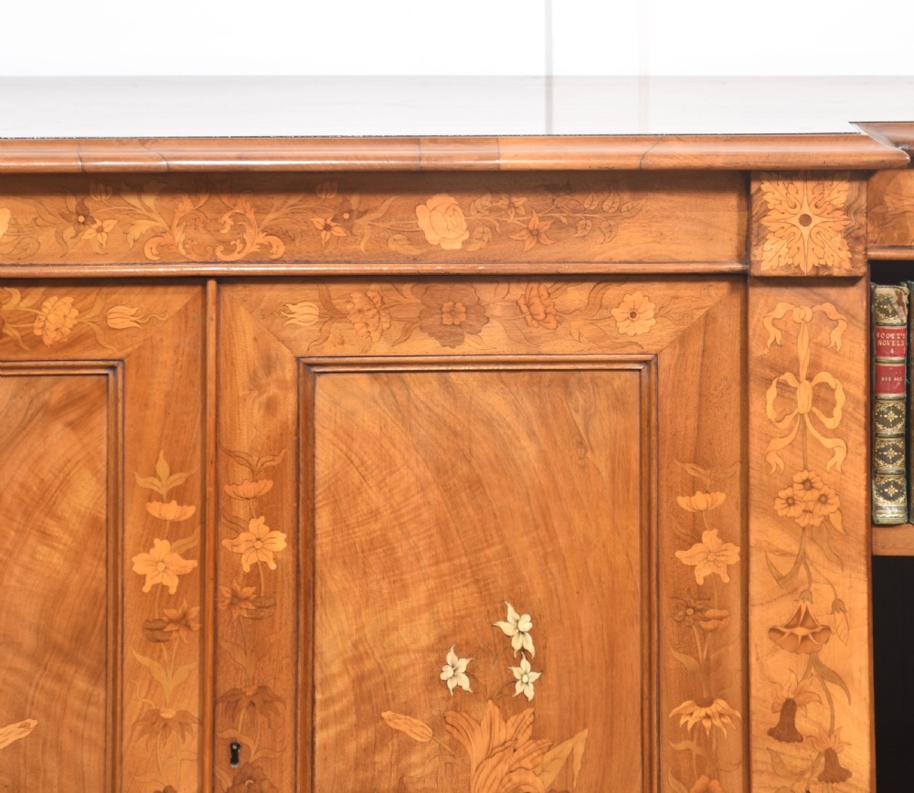 A low antique walnut breakfront bookcase featuring floral marquetry inlay across the central cupboard doors and top frieze, flanked by open adjustable shelves. View VI