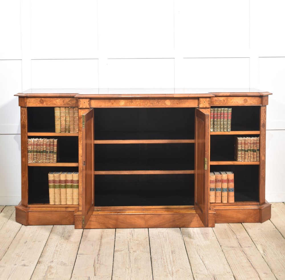 A low antique walnut breakfront bookcase featuring floral marquetry inlay across the central cupboard doors and top frieze, flanked by open adjustable shelves. View VIII