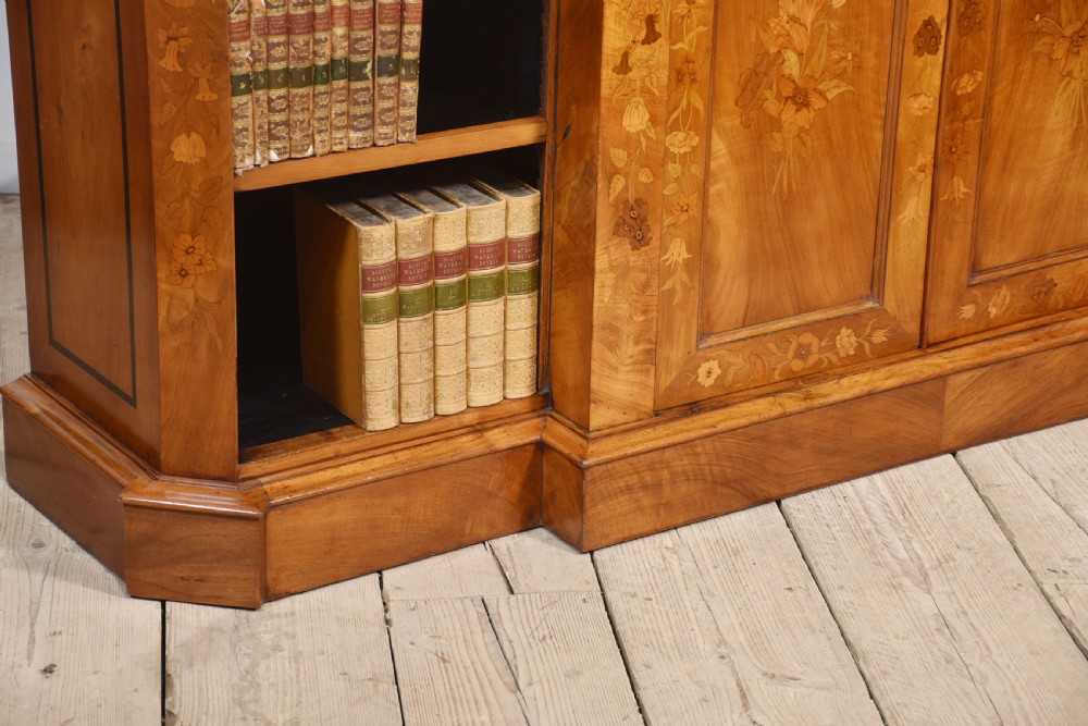 A low antique walnut breakfront bookcase featuring floral marquetry inlay across the central cupboard doors and top frieze, flanked by open adjustable shelves. View IX
