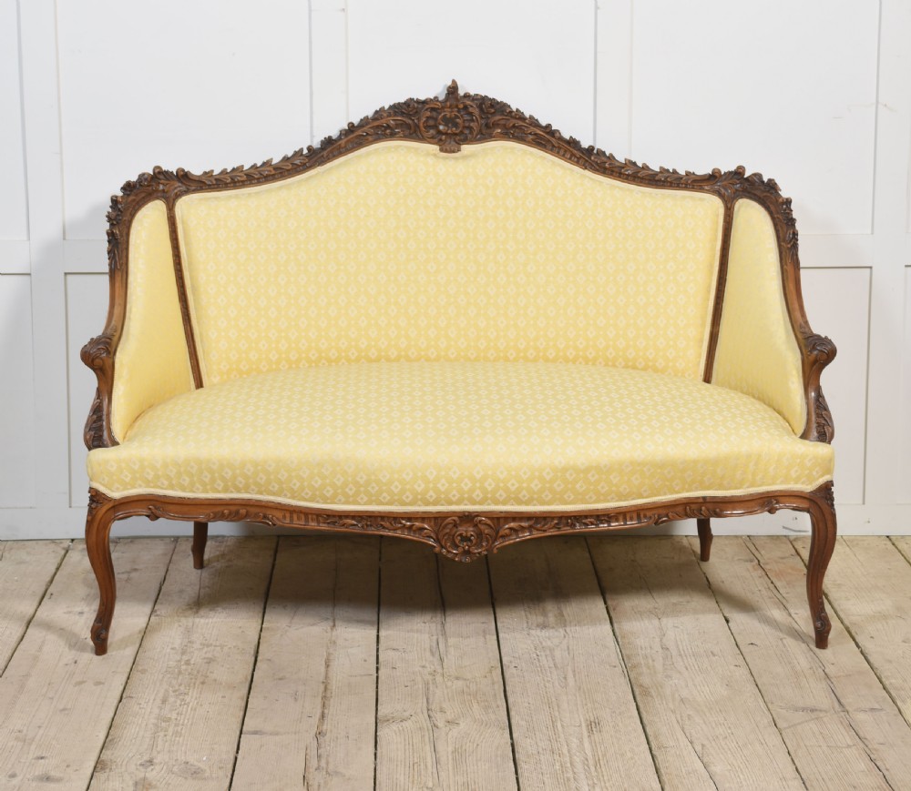 An antique carved walnut two-seater settee featuring patterned yellow upholstery, curved arms, and cabriole legs. View V