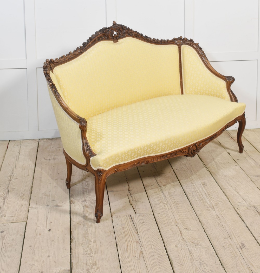 An antique carved walnut two-seater settee featuring patterned yellow upholstery, curved arms, and cabriole legs. View VII