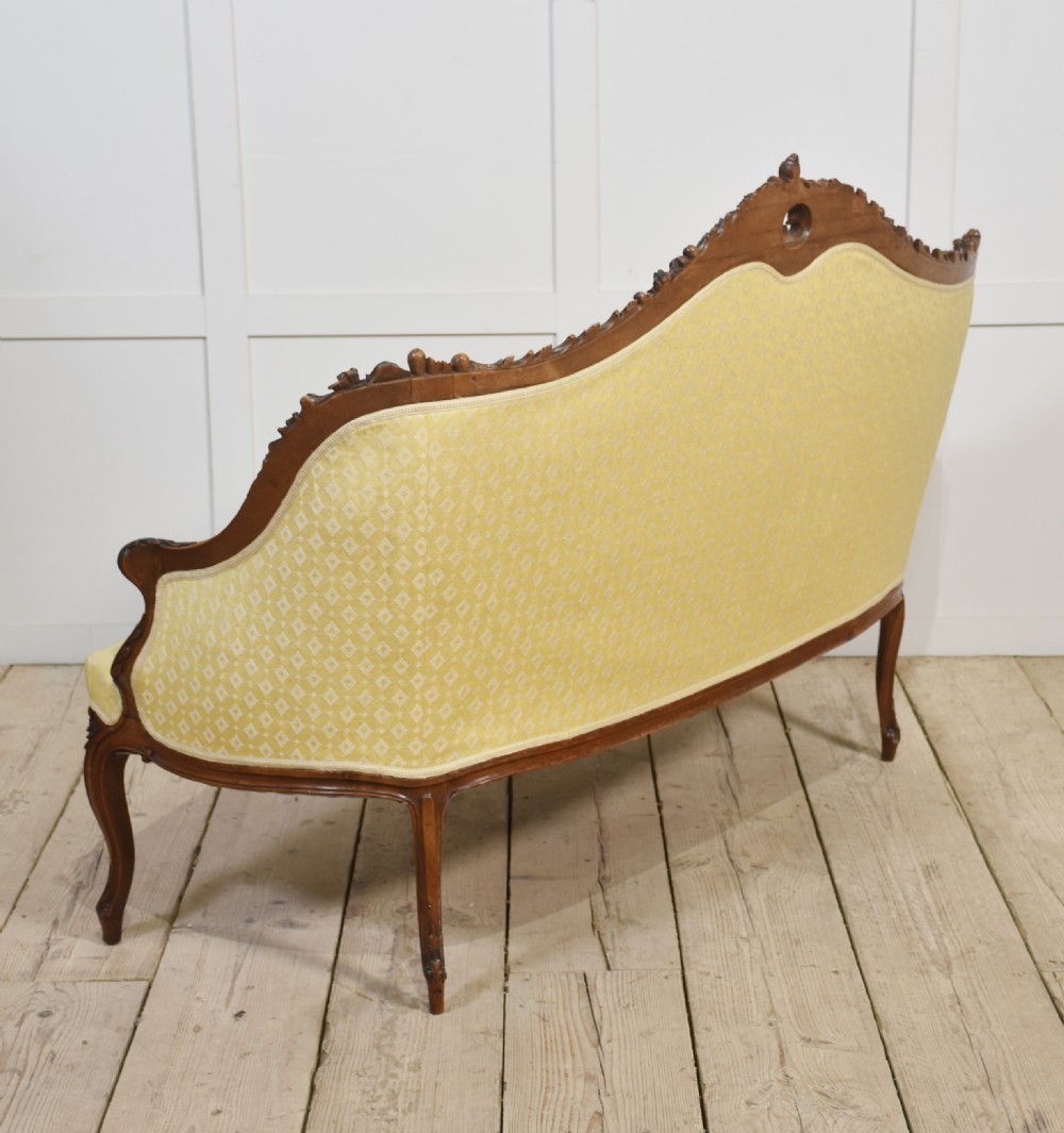 An antique carved walnut two-seater settee featuring patterned yellow upholstery, curved arms, and cabriole legs. View XV