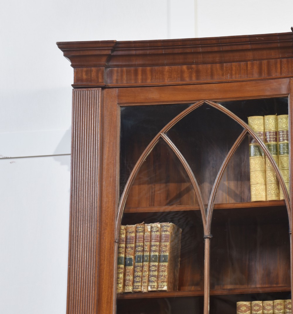 A large Regency mahogany breakfront library bookcase featuring four astragal glazed doors with Gothic arch detailing over four panelled cupboard bases. View II
