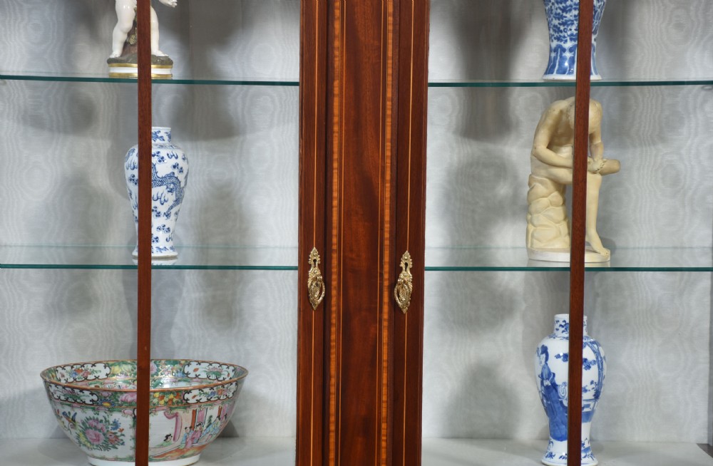 An Edwardian mahogany double bow-front display cabinet featuring glazed doors, fine satinwood inlay, glass shelves, and a lower shelf supported by tapered legs. View VIII