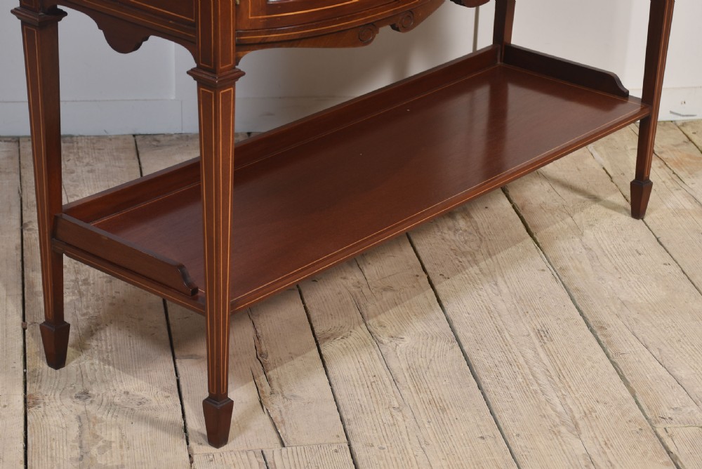 An Edwardian mahogany double bow-front display cabinet featuring glazed doors, fine satinwood inlay, glass shelves, and a lower shelf supported by tapered legs. View IX