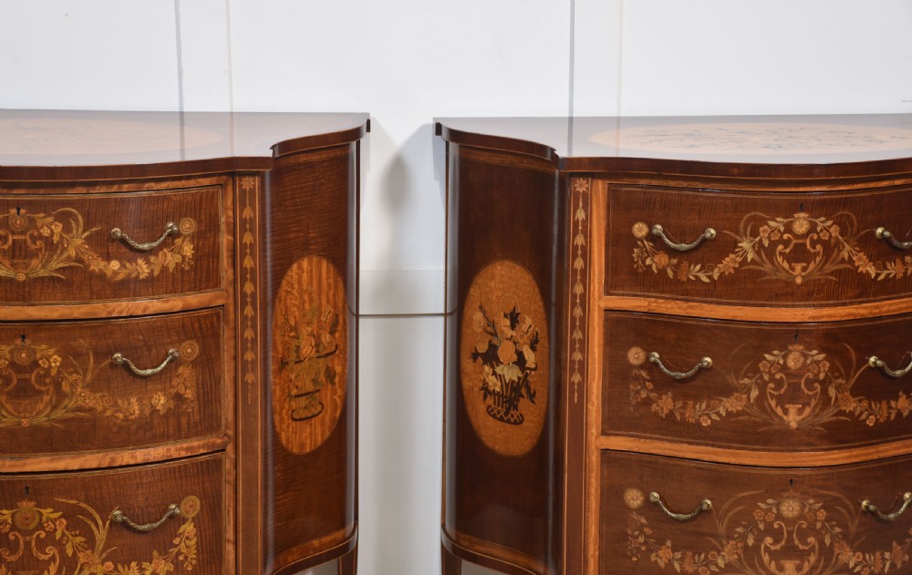 A near pair of bow-fronted mahogany chests of drawers featuring detailed floral marquetry inlay, brass handles, and slender tapered legs. View III