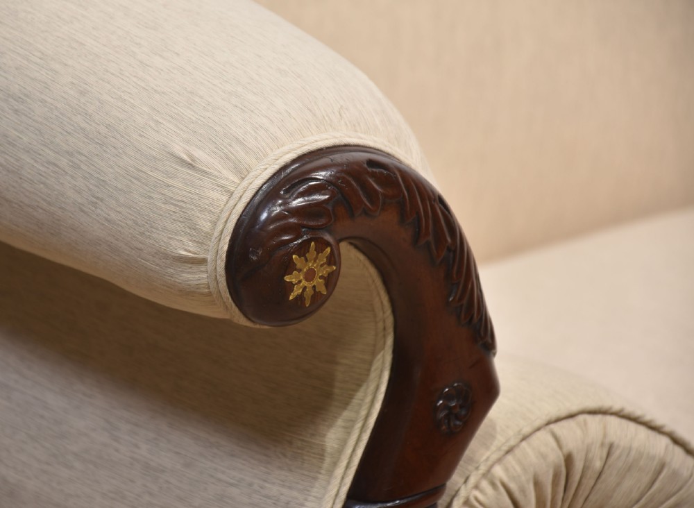 An antique Regency mahogany settee featuring brass inlay accents along the crest rail and apron, scrolled arms with matching bolster cushions, cream fabric upholstery, and turned legs on brass castors. View XII