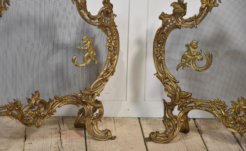 A pair of ornate Louis XV style gilt bronze fire screens featuring Rococo scrollwork, cherub mounts, and wire mesh panels on cabriole feet. View II