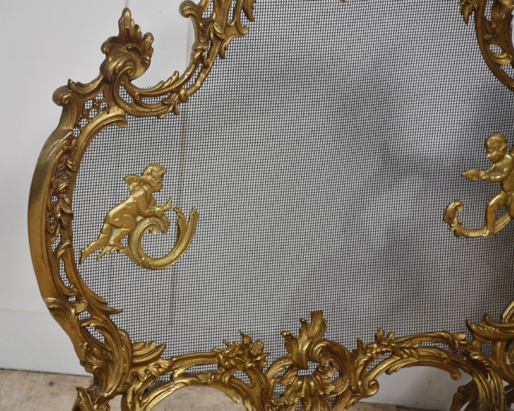 A pair of ornate Louis XV style gilt bronze fire screens featuring Rococo scrollwork, cherub mounts, and wire mesh panels on cabriole feet. View III