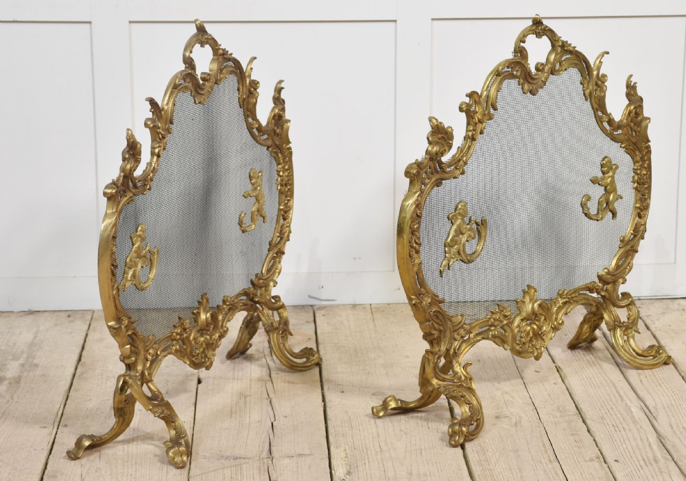 A pair of ornate Louis XV style gilt bronze fire screens featuring Rococo scrollwork, cherub mounts, and wire mesh panels on cabriole feet. View V
