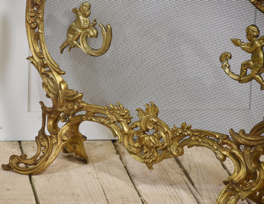 A pair of ornate Louis XV style gilt bronze fire screens featuring Rococo scrollwork, cherub mounts, and wire mesh panels on cabriole feet. View VI