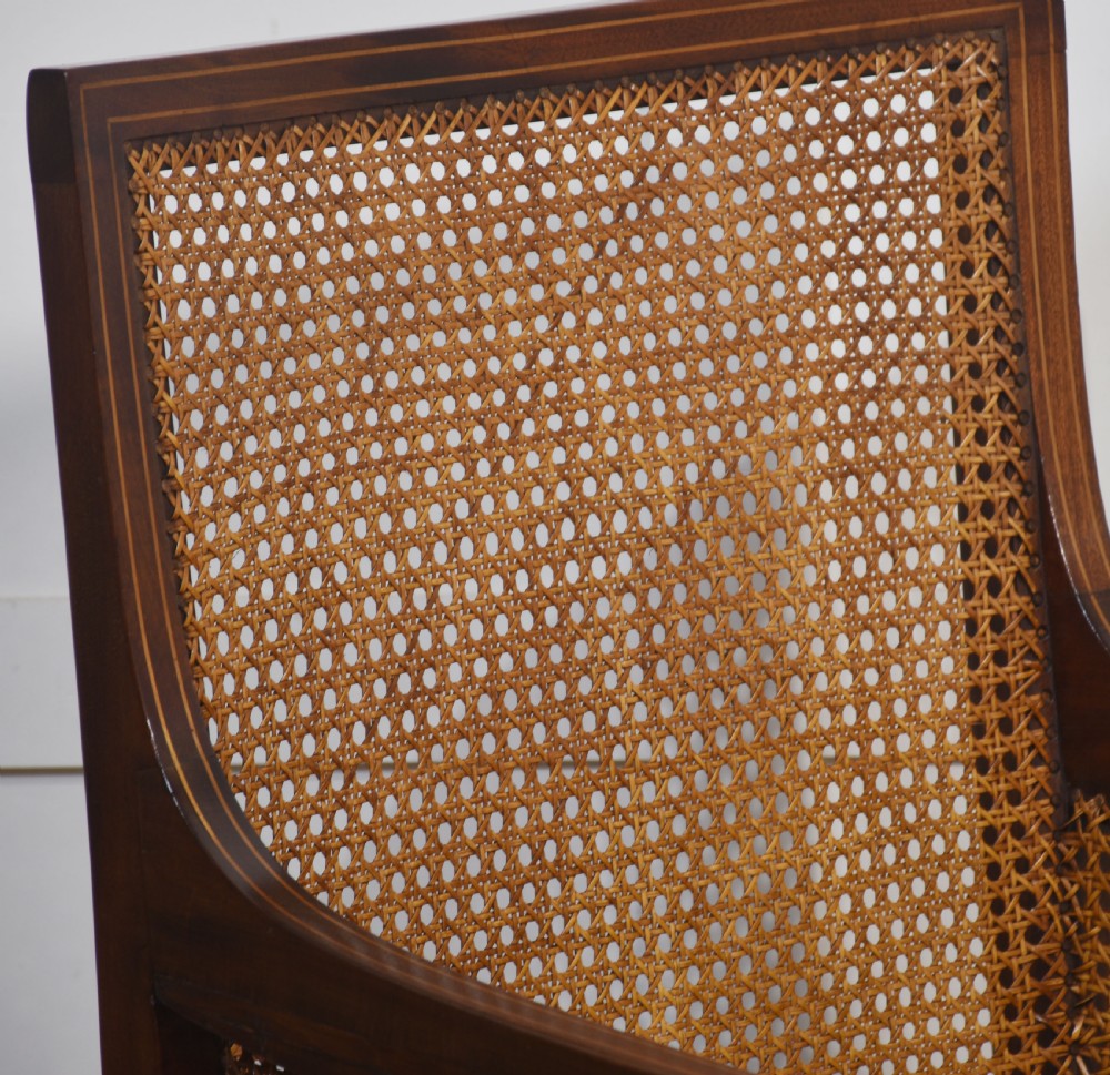 An Edwardian mahogany armchair featuring a woven cane back and sides, satinwood string inlay, turned arm supports, and a reddish-brown leather seat cushion. View III
