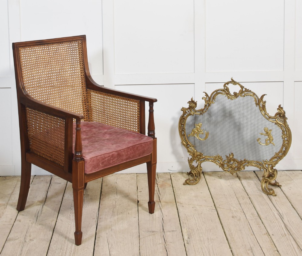 An Edwardian mahogany armchair featuring a woven cane back and sides, satinwood string inlay, turned arm supports, and a reddish-brown leather seat cushion. View V