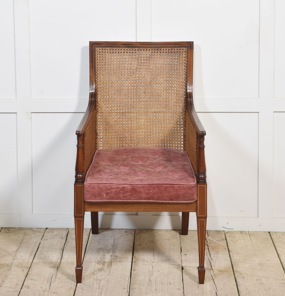 An Edwardian mahogany armchair featuring a woven cane back and sides, satinwood string inlay, turned arm supports, and a reddish-brown leather seat cushion. View VII